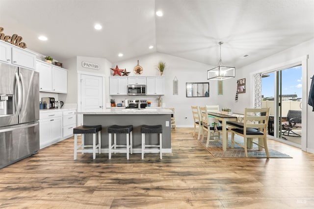 kitchen with a center island with sink, hanging light fixtures, hardwood / wood-style flooring, white cabinetry, and stainless steel appliances