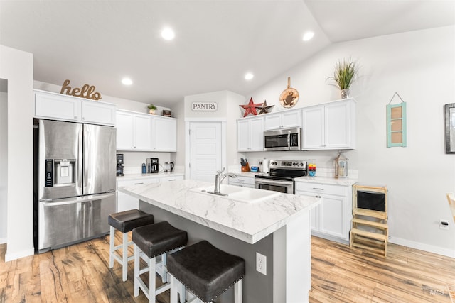 kitchen with white cabinetry, sink, stainless steel appliances, a kitchen island with sink, and a breakfast bar