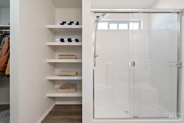 full bath featuring baseboards, a spacious closet, wood finished floors, and a shower stall