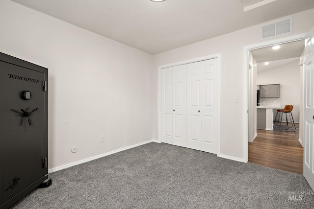 unfurnished bedroom featuring a closet, visible vents, dark carpet, and baseboards