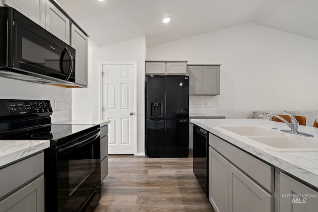 kitchen with gray cabinets, wood finished floors, vaulted ceiling, black appliances, and a sink