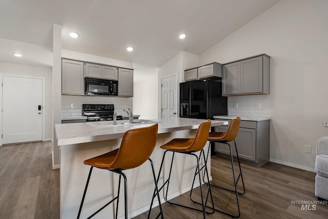 kitchen featuring tasteful backsplash, a breakfast bar, black appliances, dark wood finished floors, and gray cabinets