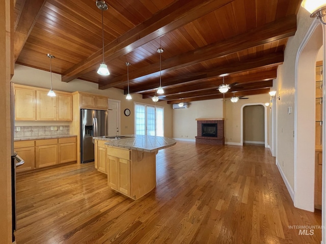 kitchen with a fireplace, light brown cabinets, ceiling fan, stainless steel fridge, and a center island with sink