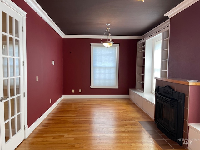 unfurnished dining area with a tiled fireplace, light wood-type flooring, and ornamental molding