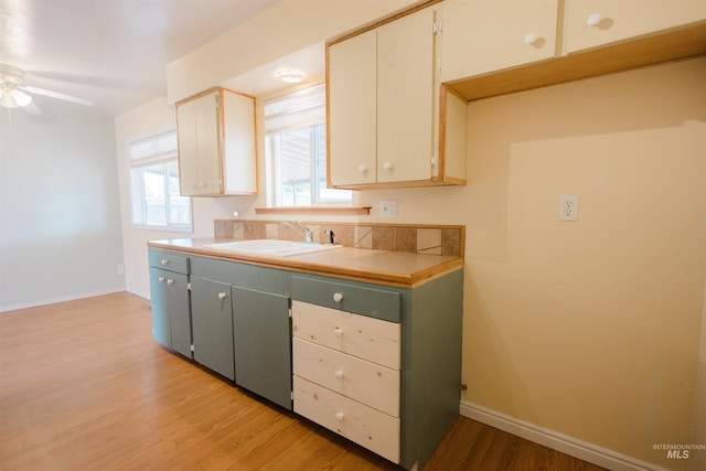 kitchen featuring a sink, a ceiling fan, light wood-style floors, baseboards, and light countertops