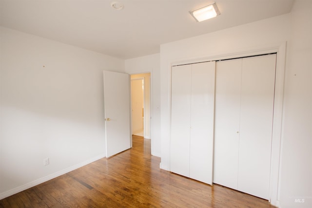 unfurnished bedroom with wood finished floors, baseboards, and a closet