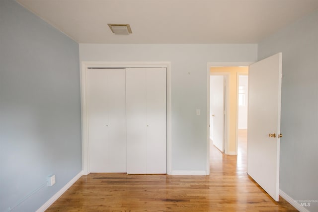 unfurnished bedroom featuring light wood finished floors, baseboards, and a closet