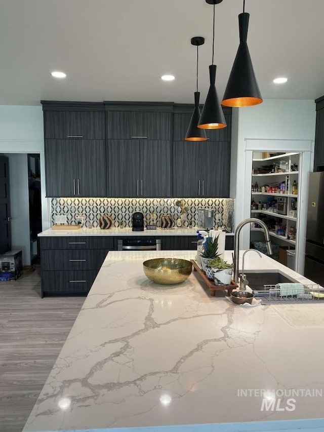 kitchen with sink, backsplash, stainless steel fridge, pendant lighting, and light hardwood / wood-style floors