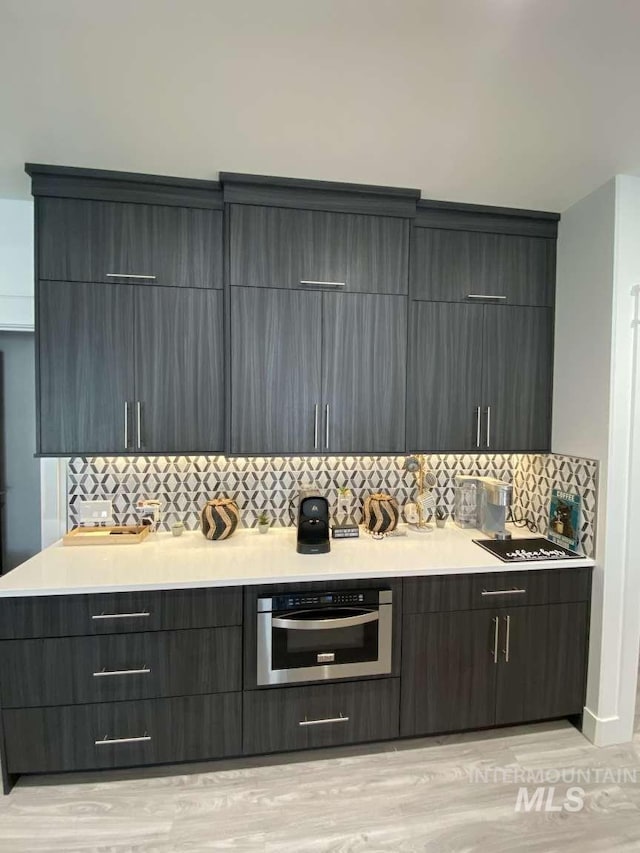 kitchen with decorative backsplash, light wood-type flooring, and stainless steel oven