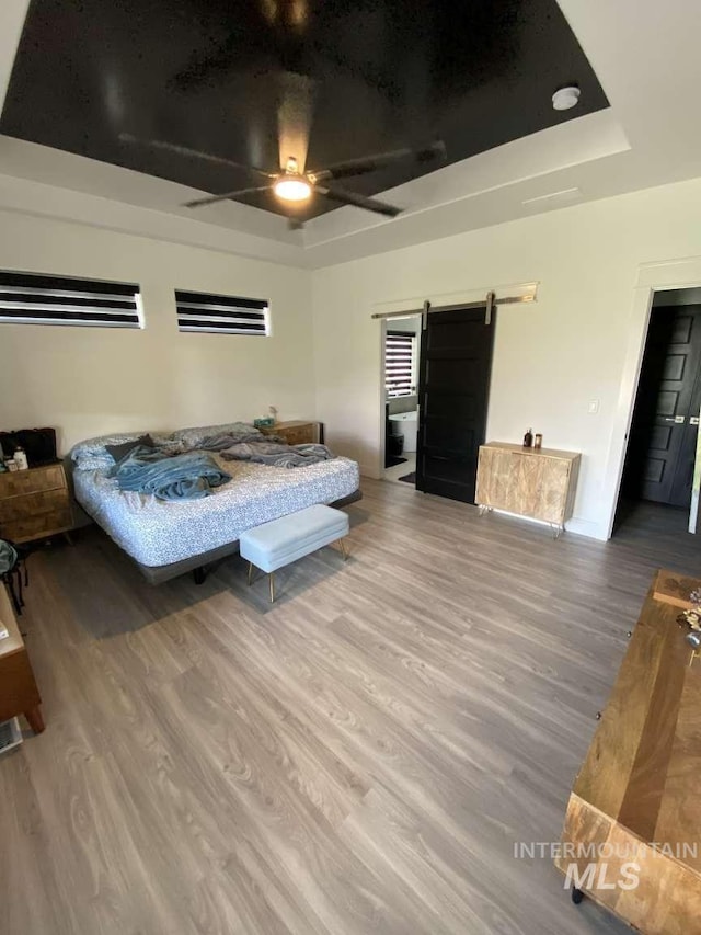 bedroom with hardwood / wood-style floors, a barn door, a raised ceiling, and ceiling fan