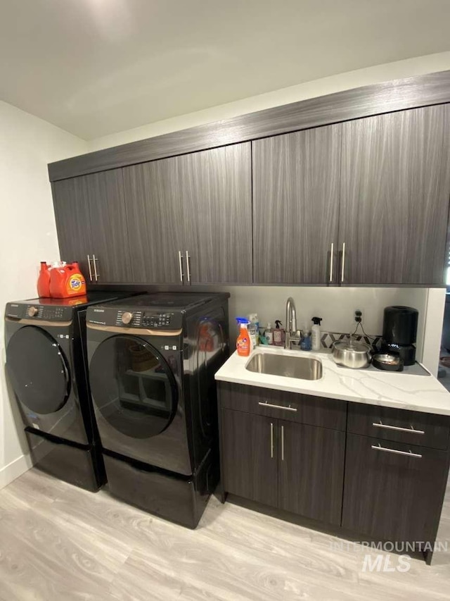 laundry area featuring washer and clothes dryer, sink, cabinets, and light wood-type flooring