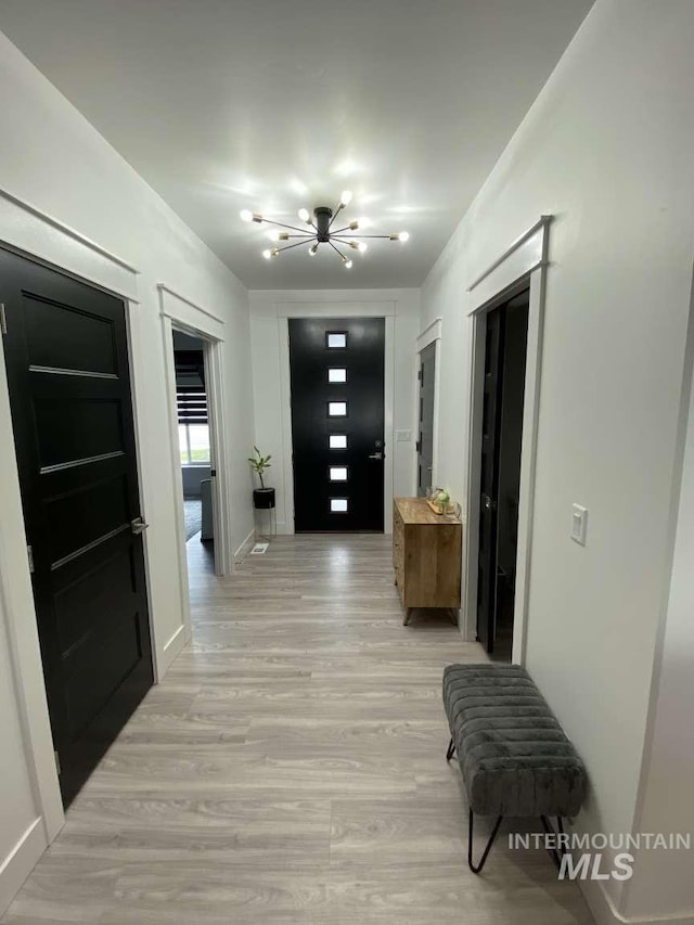 corridor with light hardwood / wood-style floors and an inviting chandelier