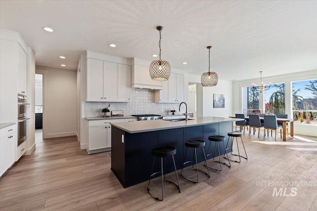 kitchen with white cabinetry, an inviting chandelier, a center island with sink, light hardwood / wood-style flooring, and decorative light fixtures