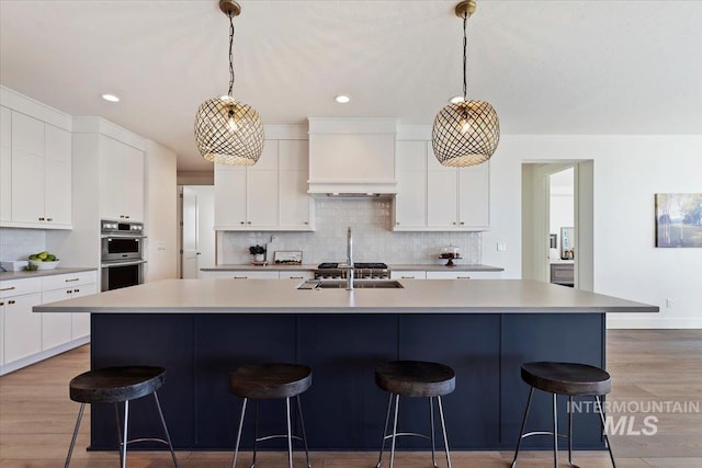 kitchen with a kitchen island with sink, white cabinetry, and hanging light fixtures