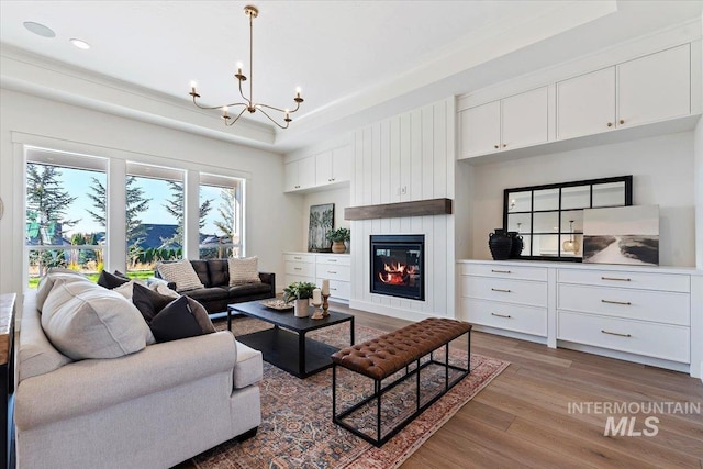 living room with a raised ceiling, a fireplace, hardwood / wood-style flooring, and a notable chandelier