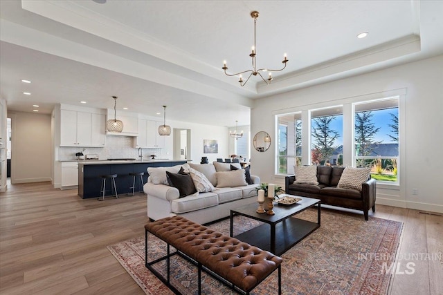 living room featuring a raised ceiling, light hardwood / wood-style floors, and a notable chandelier