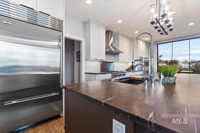 kitchen featuring tasteful backsplash, wall chimney range hood, pendant lighting, built in refrigerator, and white cabinetry