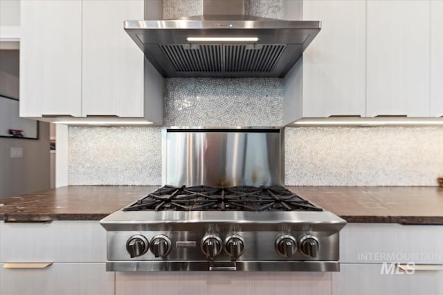 kitchen with stainless steel gas stovetop, white cabinetry, wall chimney range hood, and backsplash