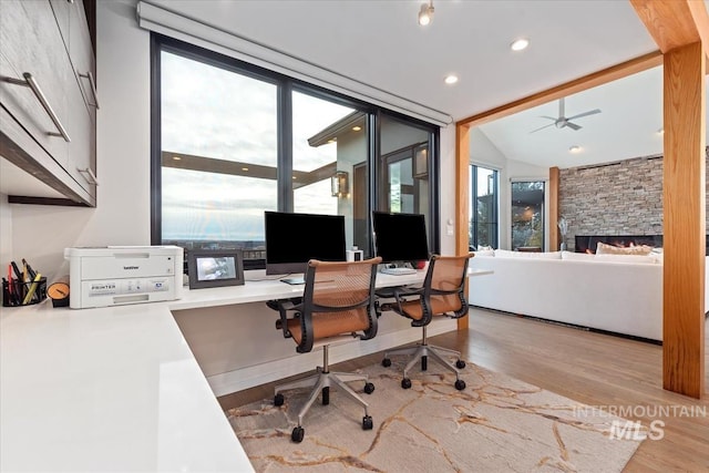 office area featuring light wood-type flooring, lofted ceiling, and a stone fireplace