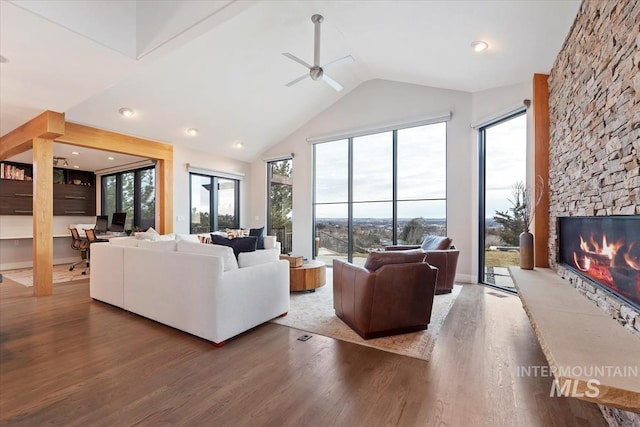 living room with ceiling fan, a stone fireplace, high vaulted ceiling, and hardwood / wood-style floors