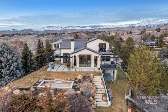 rear view of house with a lawn, a balcony, a mountain view, a pergola, and a patio