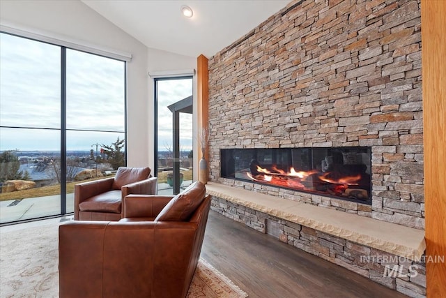 living room featuring a water view, a stone fireplace, vaulted ceiling, and wood-type flooring