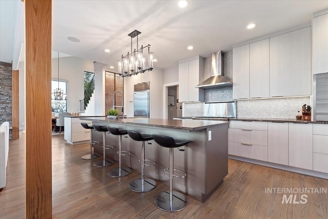 kitchen featuring a large island, dark wood-type flooring, wall chimney exhaust hood, white cabinets, and built in refrigerator