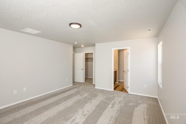 unfurnished bedroom with a spacious closet, light carpet, a closet, and a textured ceiling