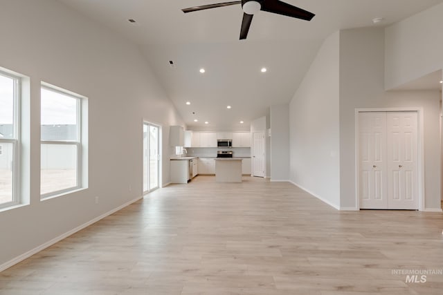 unfurnished living room featuring sink, light hardwood / wood-style floors, high vaulted ceiling, and ceiling fan