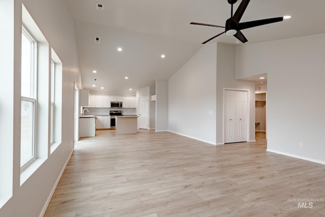 unfurnished living room with ceiling fan, high vaulted ceiling, sink, and light wood-type flooring