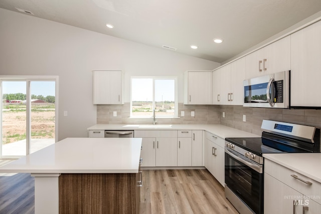 kitchen with appliances with stainless steel finishes, lofted ceiling, white cabinets, and a wealth of natural light