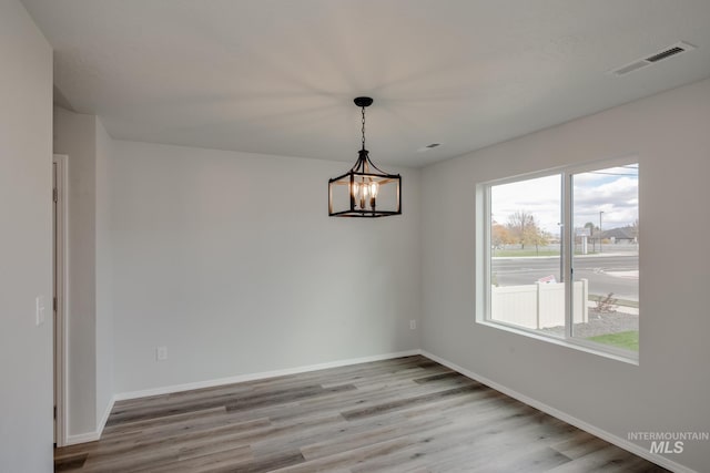 unfurnished room featuring a notable chandelier, baseboards, visible vents, and wood finished floors