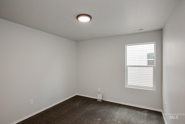 empty room with baseboards, visible vents, dark colored carpet, and a textured ceiling