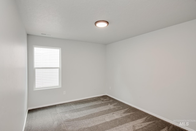 carpeted spare room featuring a textured ceiling and baseboards