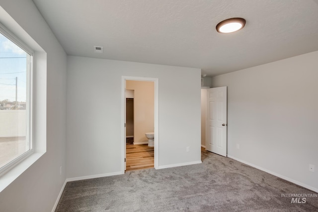 unfurnished bedroom with carpet, visible vents, baseboards, and ensuite bathroom