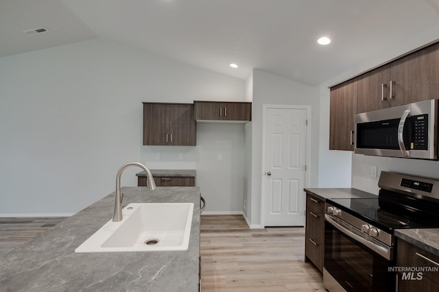 kitchen featuring lofted ceiling, light wood-style flooring, a sink, appliances with stainless steel finishes, and modern cabinets