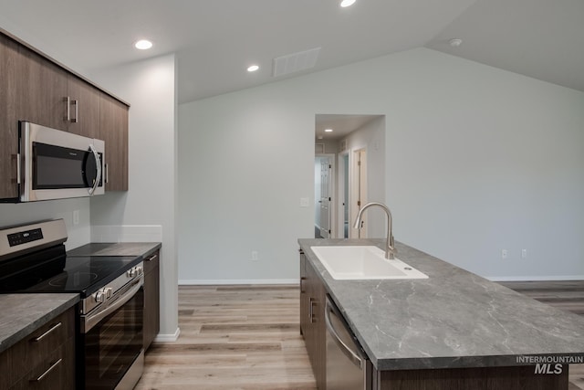 kitchen with light wood-type flooring, a kitchen island with sink, stainless steel appliances, and a sink