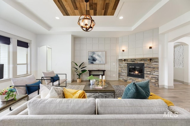 living area featuring an inviting chandelier, a fireplace, light wood-style floors, arched walkways, and a tray ceiling
