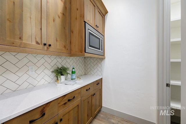 kitchen featuring backsplash, light countertops, baseboards, stainless steel microwave, and light wood-style flooring
