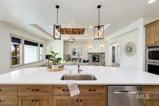 kitchen with a stone fireplace, open floor plan, light countertops, a sink, and appliances with stainless steel finishes