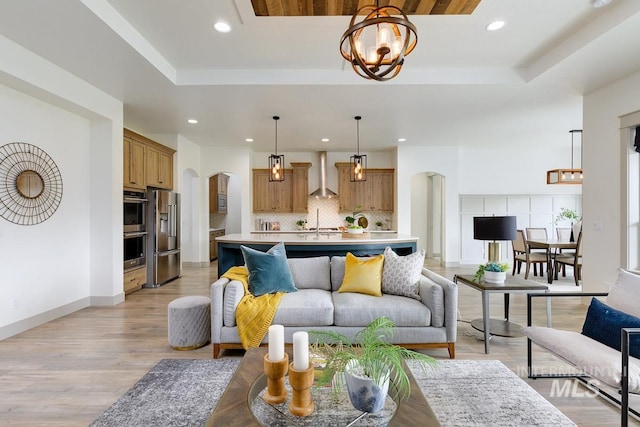 living area featuring arched walkways, a tray ceiling, an inviting chandelier, and recessed lighting