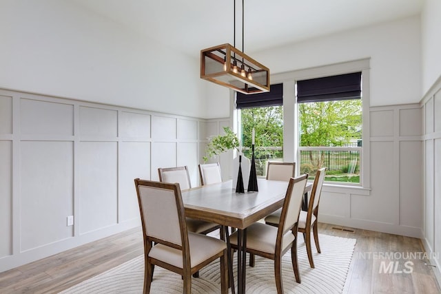 dining room with visible vents, a wainscoted wall, light wood finished floors, an inviting chandelier, and a decorative wall