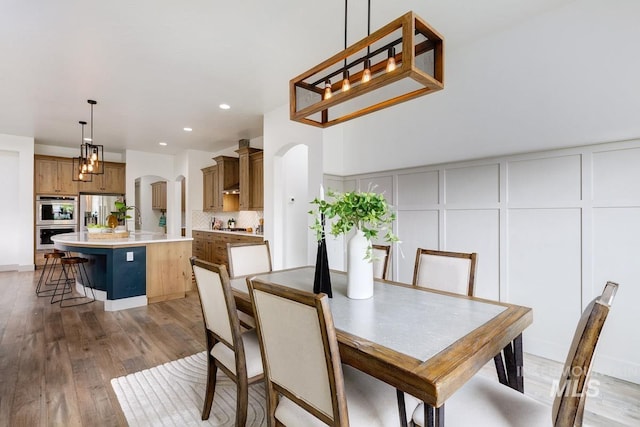 dining area with light wood-type flooring, arched walkways, a decorative wall, and recessed lighting