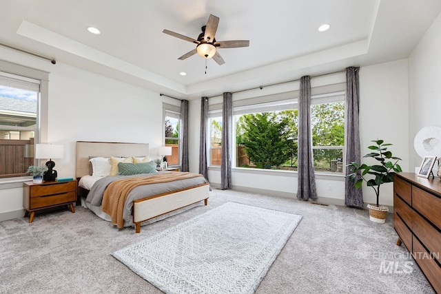 bedroom with multiple windows, a tray ceiling, recessed lighting, and light colored carpet