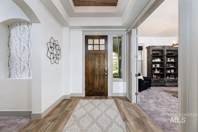 entryway with arched walkways, baseboards, wood finished floors, and a raised ceiling