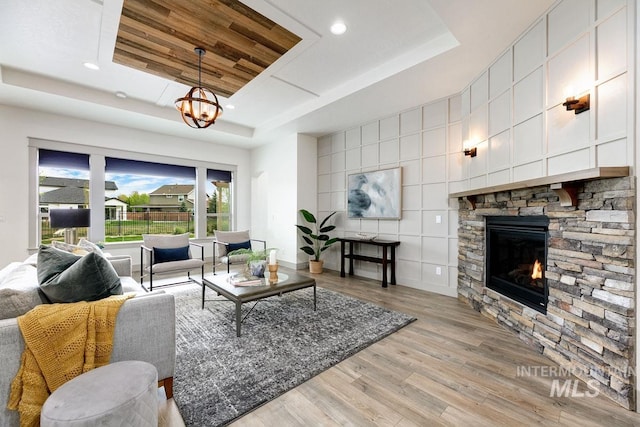 living room with a fireplace, a raised ceiling, a notable chandelier, recessed lighting, and light wood-style flooring
