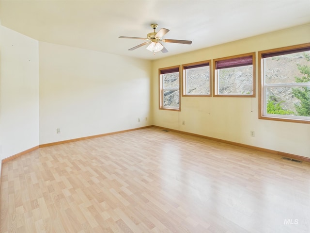 empty room featuring plenty of natural light, light wood finished floors, ceiling fan, and baseboards