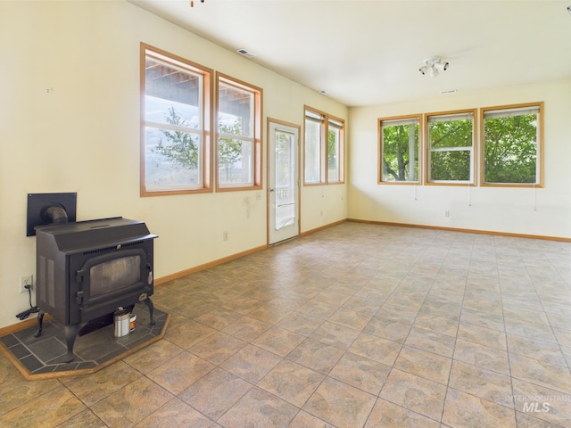 unfurnished living room with baseboards, a wood stove, and visible vents