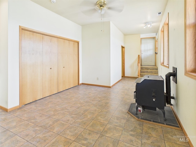 interior space featuring a closet, baseboards, ceiling fan, and a wood stove