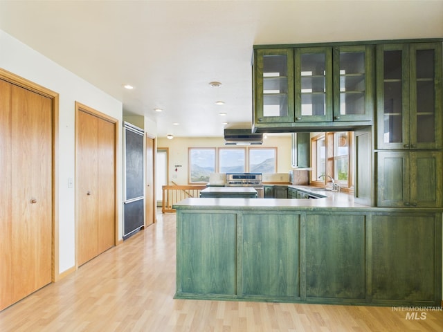 kitchen with glass insert cabinets, a sink, a peninsula, light wood-style floors, and green cabinetry